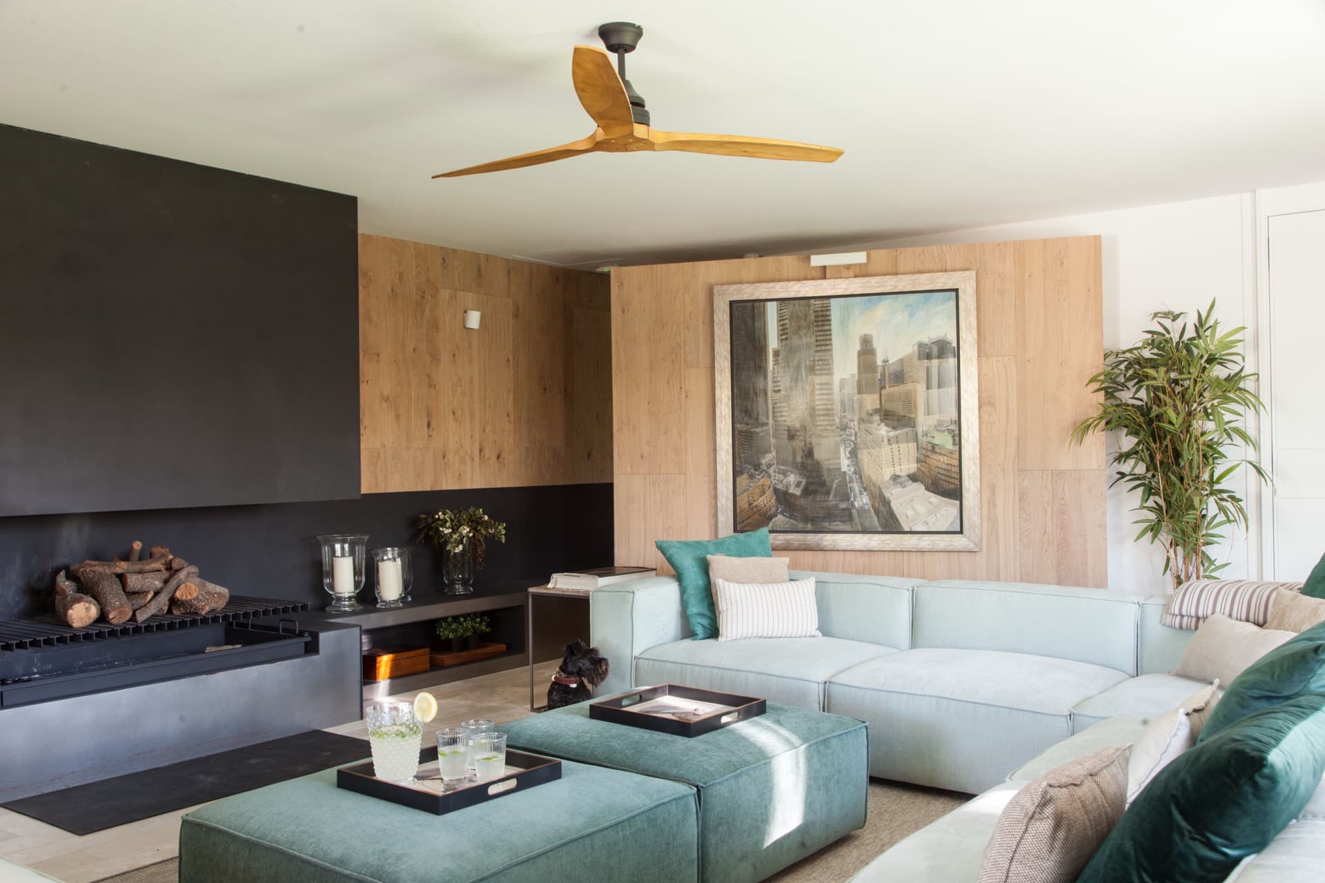 Salón con revestimiento de roble, chimenea negra y sofás verde agua