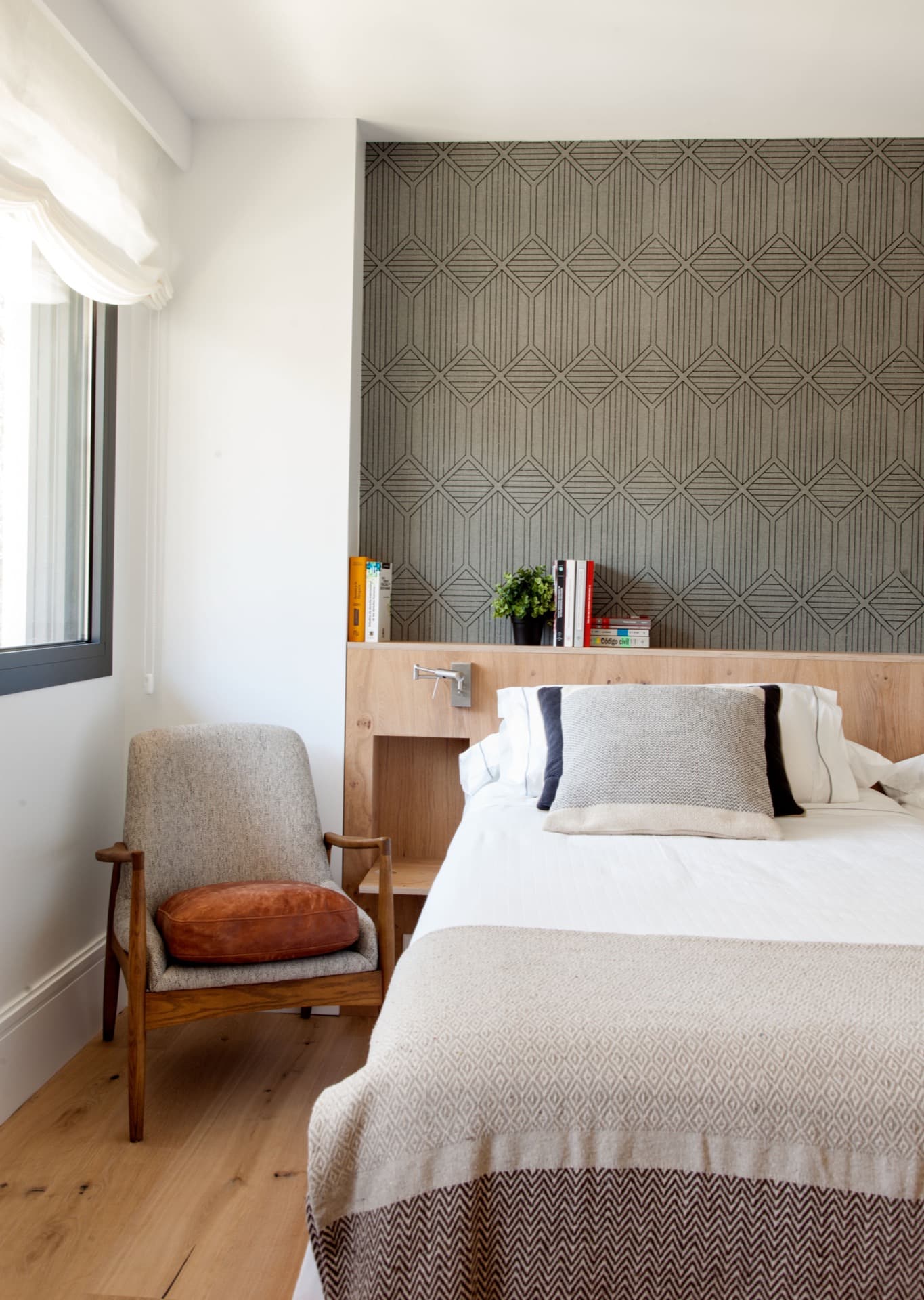 Dormitorio con cabecero de madera, butaca y textiles geométricos